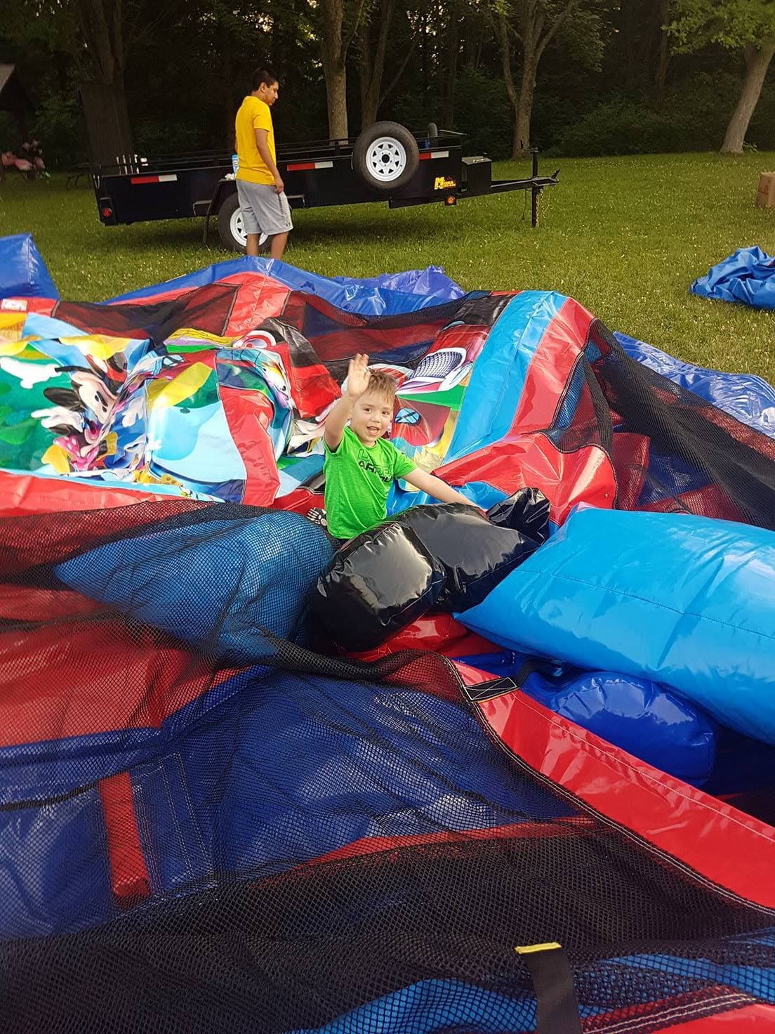 A child waving with a big smile at an outdoor bouncy castle setup