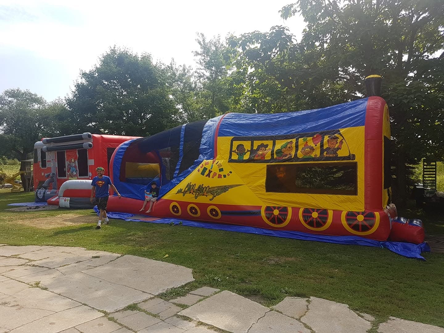 The Train Combo bouncy castle set up on grass with a firetruck castle behind